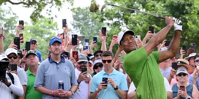 Mark Radetic holds his beer instead of a cellphone as Tiger Woods plays a shot during the PGA Championship on May 20, 2022 in Tulsa, Oklahoma.