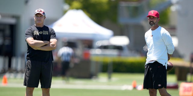 San Francisco 49ers general manager John Lynch, left, and head coach Kyle Shanahan watch players warm up at the team's practice facility in Santa Clara, Calif., on June 1, 2022.