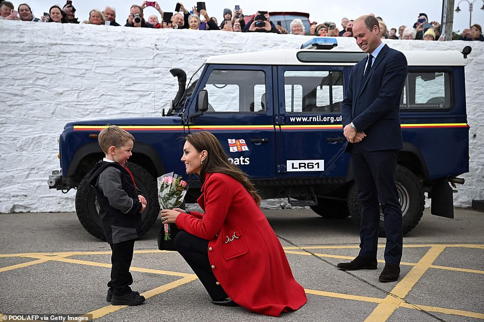 Prince William watches as his wife Catherine, Princess of Wales is presented with a posy of flowers by four-year-old Theo Crompton during their visit to the RNLI