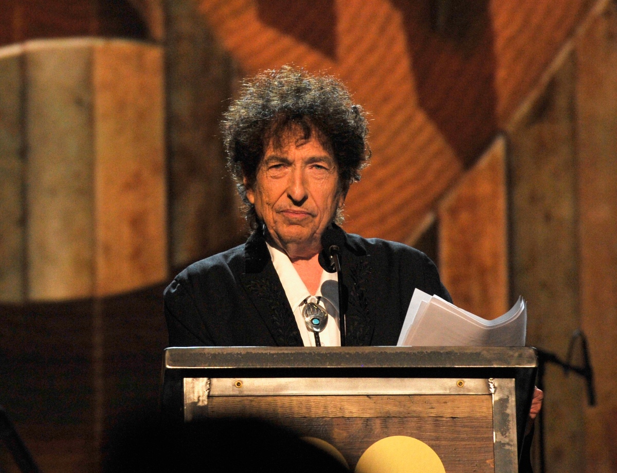 Bob Dylan holds papers and stands at a podium.
