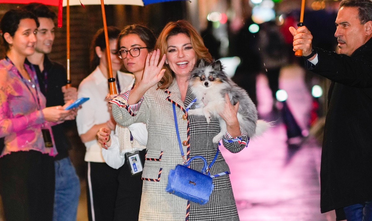 Shania Twain waves and smiles while holding her dog. 