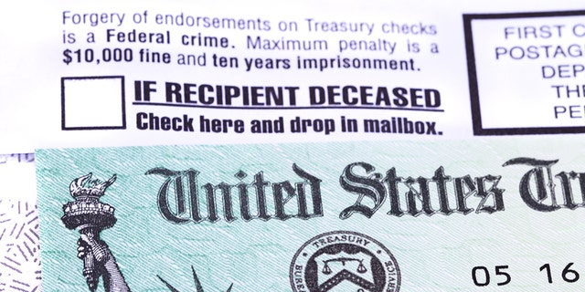 A United States government Treasury Check used to pay Social Security or Medicare benefits lies on top of the opened envelope used to mail it to the recipient. The envelope has warnings of criminal penalties for anyone who fraudulently endorses the check. It also warns that if the recipient is deceased, the check should be placed in the return mail. The distinctive green checks feature an engraving of the Statue of Liberty and the Treasury Seal.