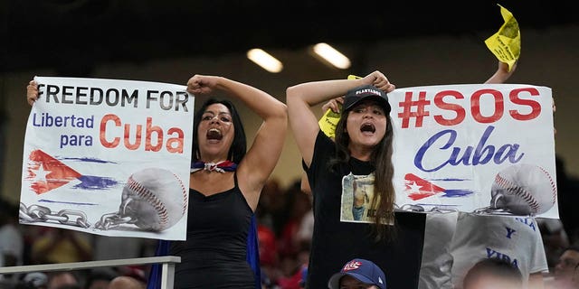 Demonstrators hold up signs and chant during the sixth inning of a World Baseball Classic game between Cuba and the U.S., Sunday, March 19, 2023, in Miami.