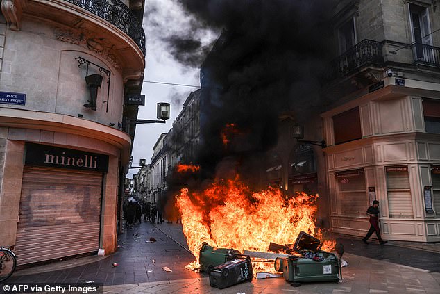 A man walks past a fire made of matresses and waste containers amid a demonstration in Bordeaux, southwestern France, on March 18, 2023