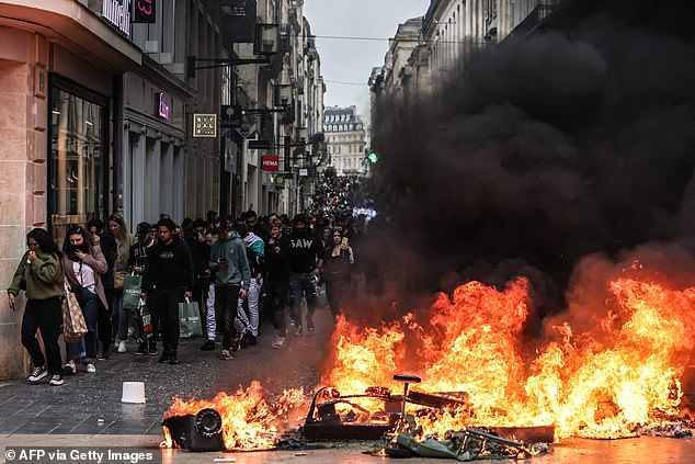 Pedestrians react as they walk past a fire made of household waste containers during a demonstration in Bordeaux, southwestern France, on March 18, 2023