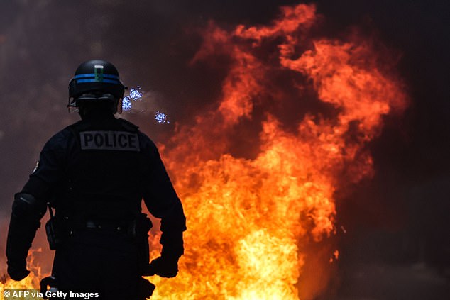 A French police officer in riot gear stands next to a fire during a demonstration in Bordeaux, southwestern France, on March 18, 2023