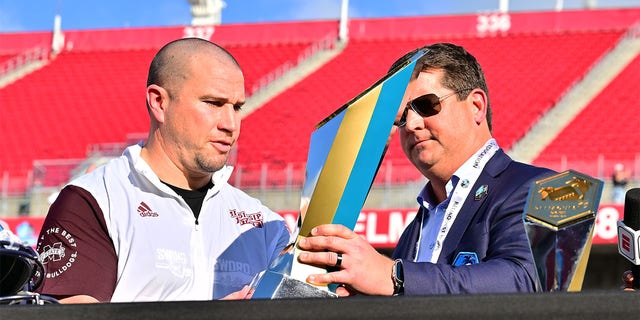 ReliaQuest CEO Brian Murphy, right, presents Mississippi State Bulldogs head coach Zach Arnett the trophy after defeating the Illinois Fighting Illini 19-10 in the ReliaQuest Bowl at Raymond James Stadium on Jan. 2, 2023 in Tampa, Florida.