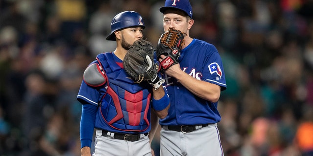 Catcher Isiah Kiner-Falefa and starting pitcher Adrian Sampson of the Texas Rangers meet at the pitcher's mound during a game against the Seattle Mariners at Safeco Field Sept. 29, 2018, in Seattle.