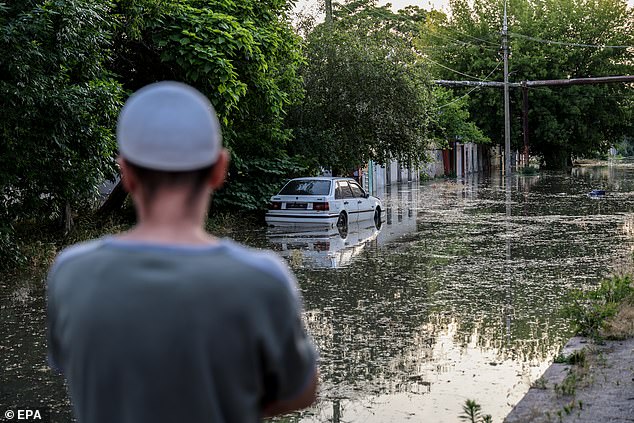 A man looks on as a car is parked in a flooded street of Kherson, Ukraine on Tuesday