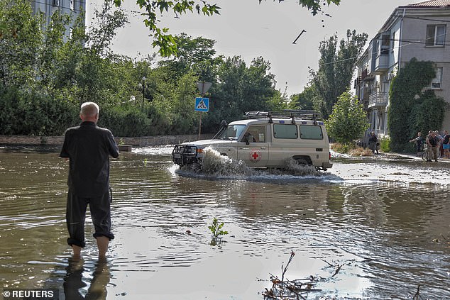 Red Cross volunteers drive a car on a flooded street on Tuesday after the Nova Kakhovka dam breached in Kherson, Ukraine