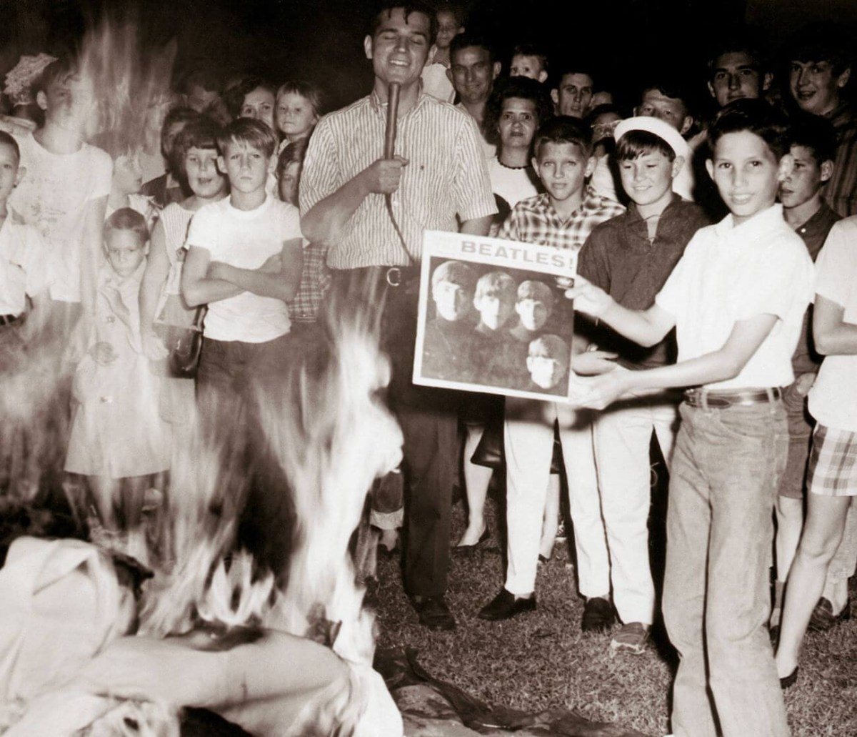 A black and white picture of a teenager burning a Beatles album in front of a crowd.