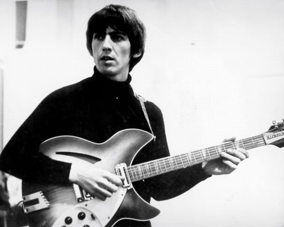 A black and white picture of George Harrison playing guitar.
