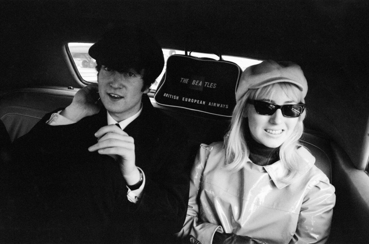 A black and white picture of John Lennon and Cynthia Lennon wearing hats and sitting in the back of a car.
