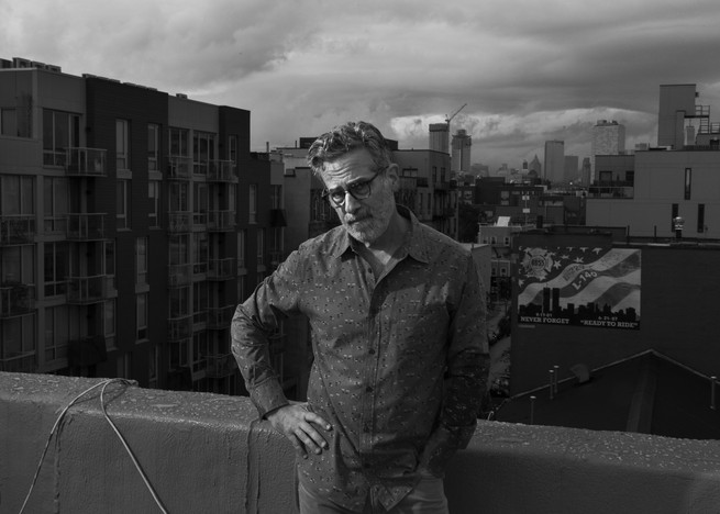 BW image of a man on a rooftop looking at the camera with his hand on his hip