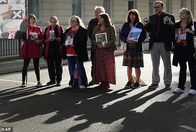Sir Patrick also accused an unnamed official of 'completely rewriting' scientific advice on social distancing, the Covid-19 inquiry in London heard today. Pictured, bereaved families holding pictures of their loved ones as they stand outside the opening hearing of module two of the Covid Inquiry in London today