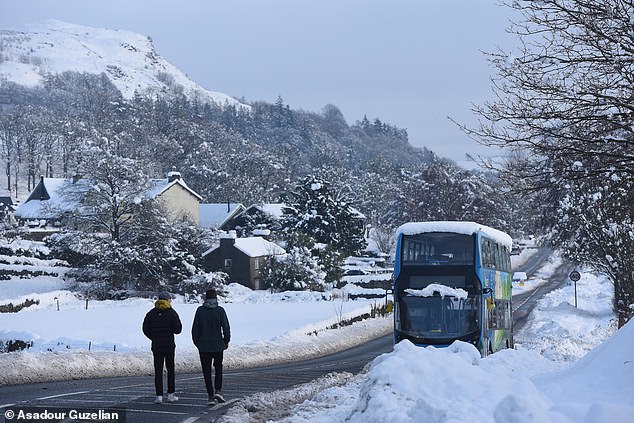 Walkers approach an abandoned bus on the A591 between Kendal and Windermere following heavy snowfall
