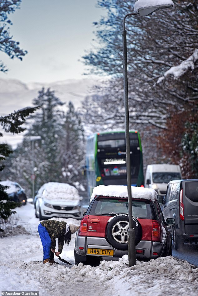A woman clears snow from around her car on the A591 in Windermere after heavy snow falls