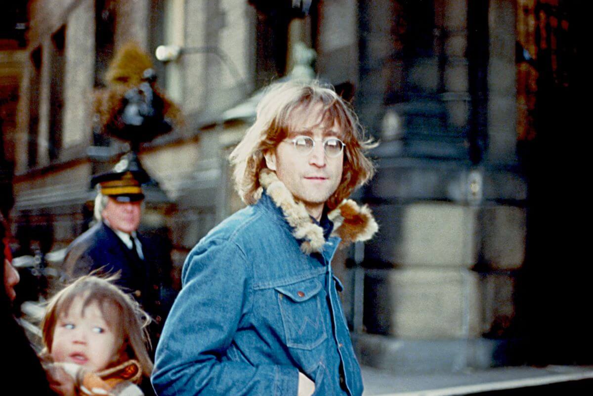 John Lennon wears a denim jacket with a fur collar and walks outside.