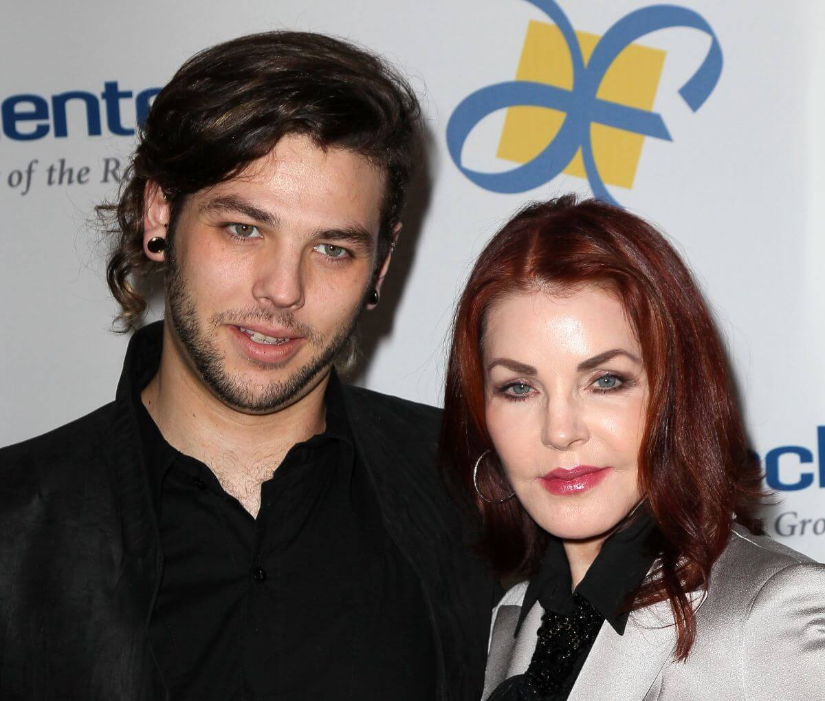 Priscilla Presley wears a silver jacket and stands with her son Navarone Garvia, who wears a black shirt.